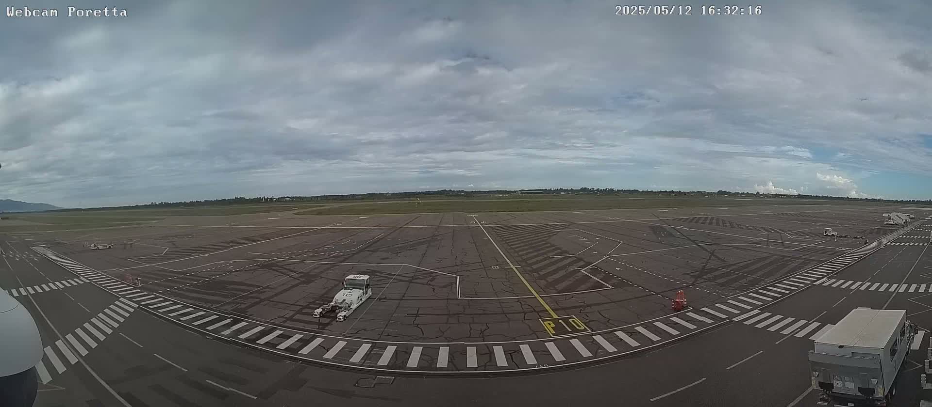 A mostly cloudy day overlooks an airport tarmac with several service vehicles parked and a few jet bridges visible in the distance.