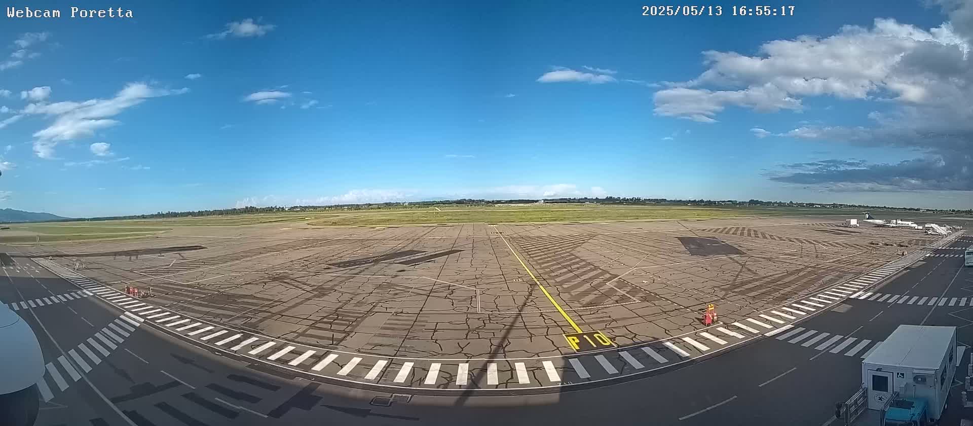 A mostly sunny day at an airport tarmac shows a cracked asphalt surface with marked taxiways and a distant airplane.