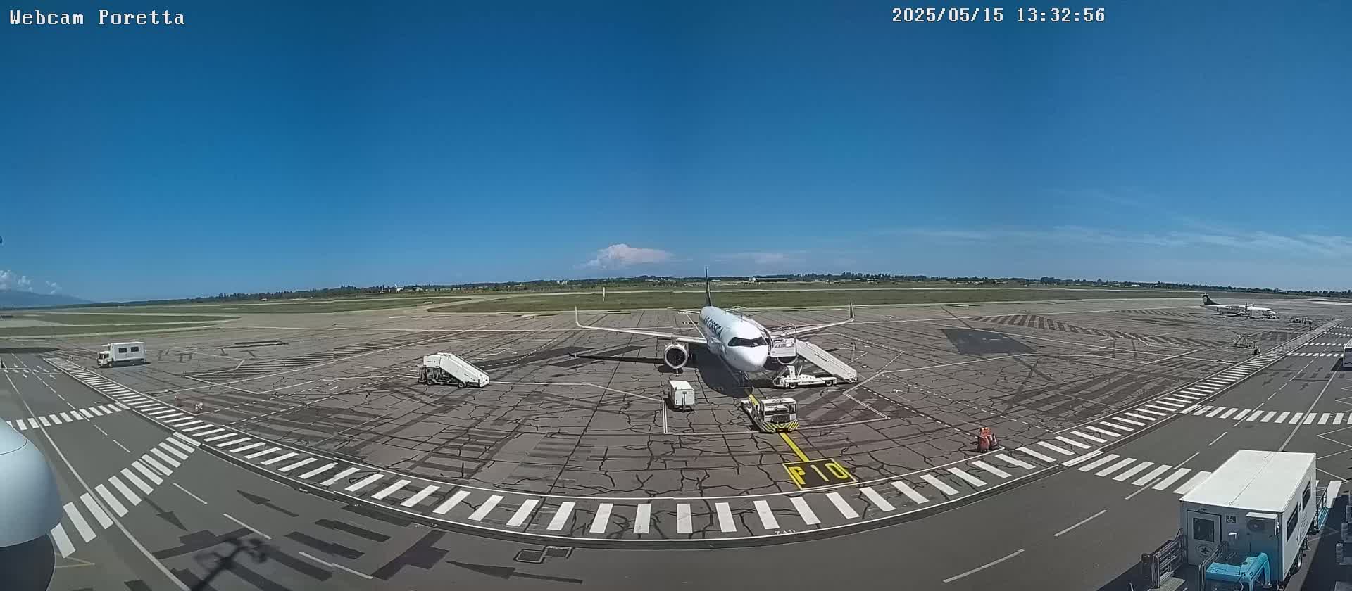 A passenger airplane is parked at an airport tarmac on a sunny day with a mostly clear blue sky.