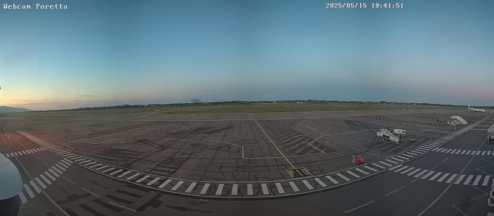 An airport tarmac at dusk with a few service vehicles and one airplane visible in the distance under a clear sky.