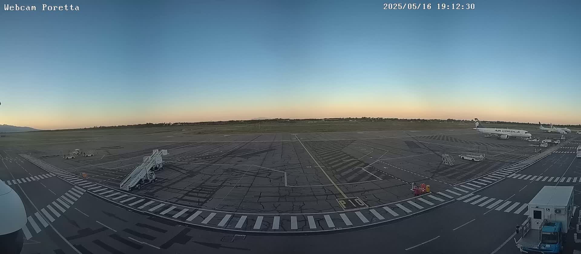 An airport tarmac at dusk with several planes and ground support equipment visible under a clear sky.