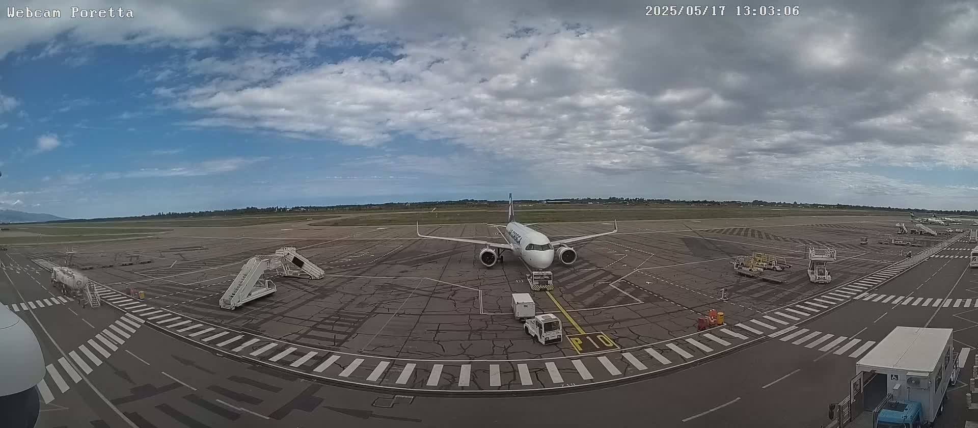 A passenger airplane sits on the tarmac of an airport under a partly cloudy sky.