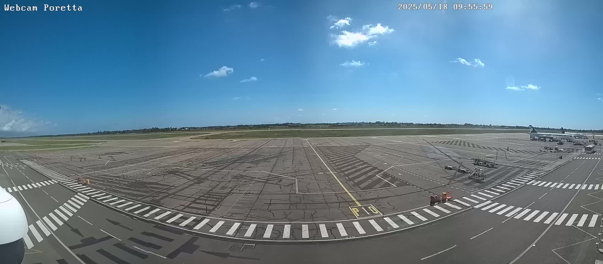 A mostly sunny airport tarmac with several airplanes parked near a gate, and service vehicles present.