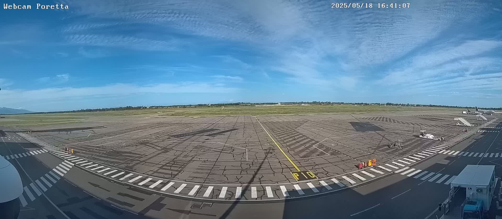 A mostly sunny day at an airport tarmac shows several service vehicles and a plane in the distance.