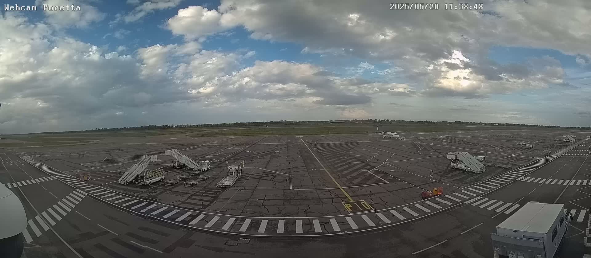 An airport tarmac with several airplanes, jet bridges, and ground support equipment under a partly cloudy sky.