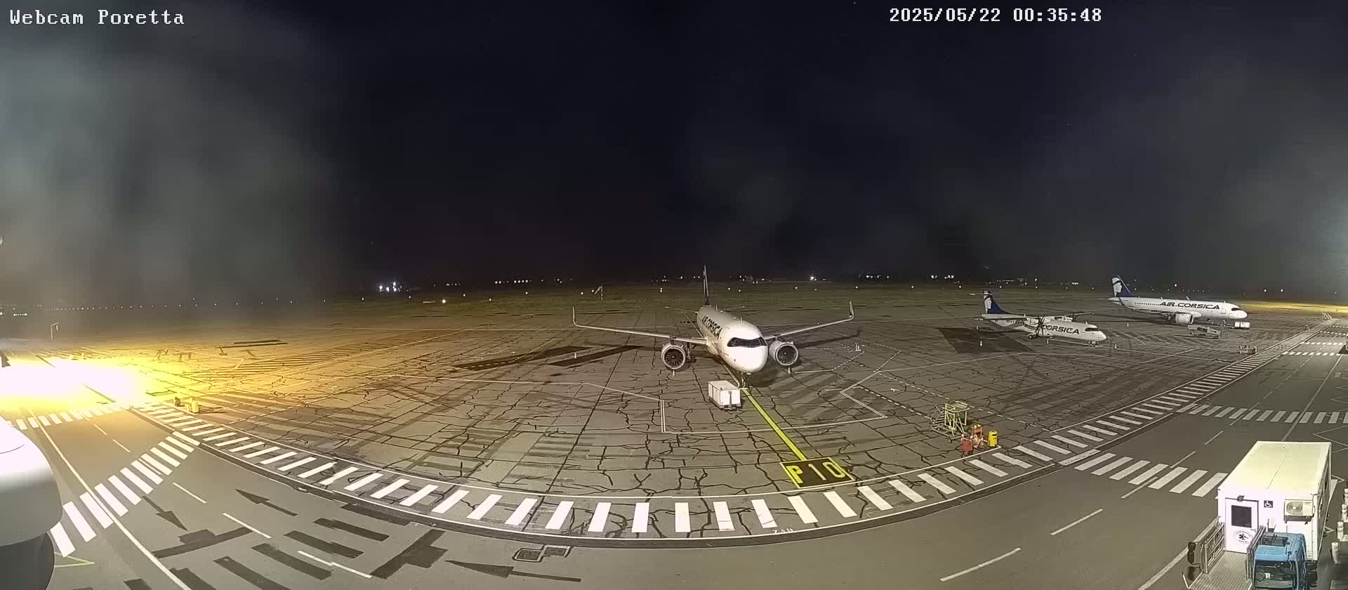 At night, on an airport tarmac, three airplanes are parked, one of which is significantly larger than the others, under a mostly clear, dark sky.