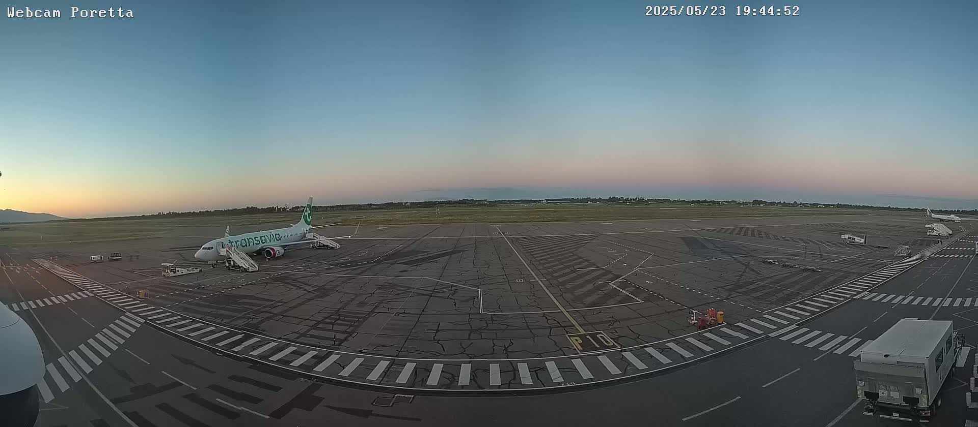 An airplane sits on an airport tarmac at dusk under a clear, twilight sky.