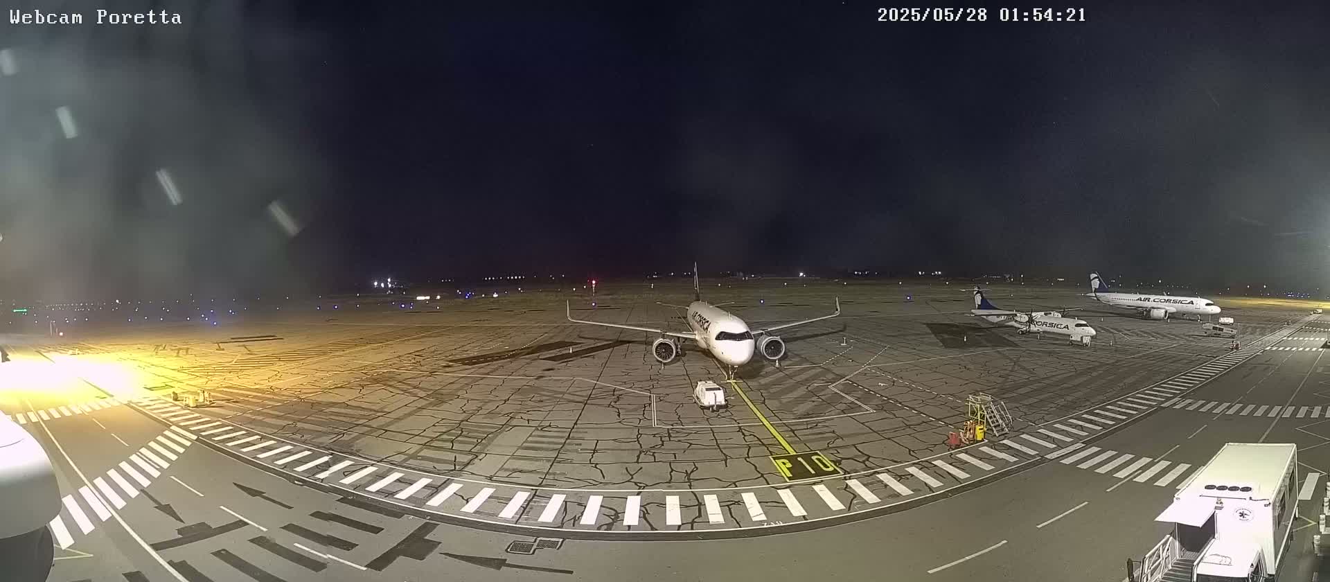 At night, under light snow, several airplanes are parked on a tarmac at an airport.
