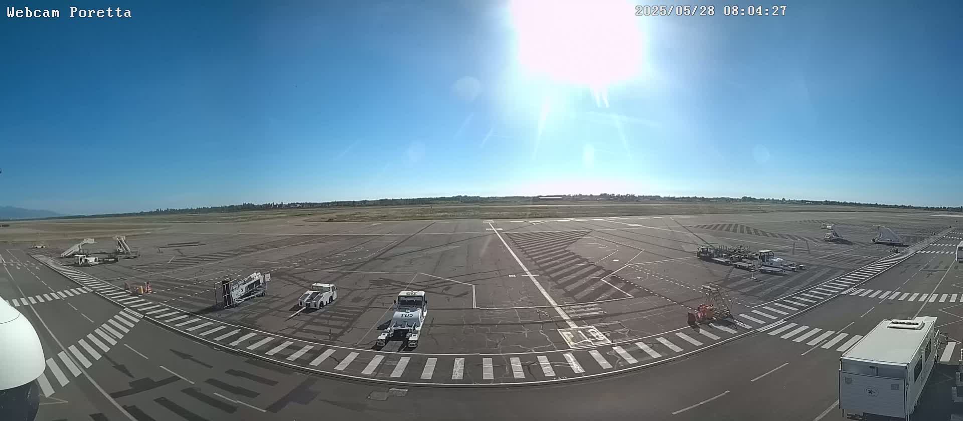 A sunny day at an airport tarmac shows several ground support vehicles and a white van parked near crosswalks.