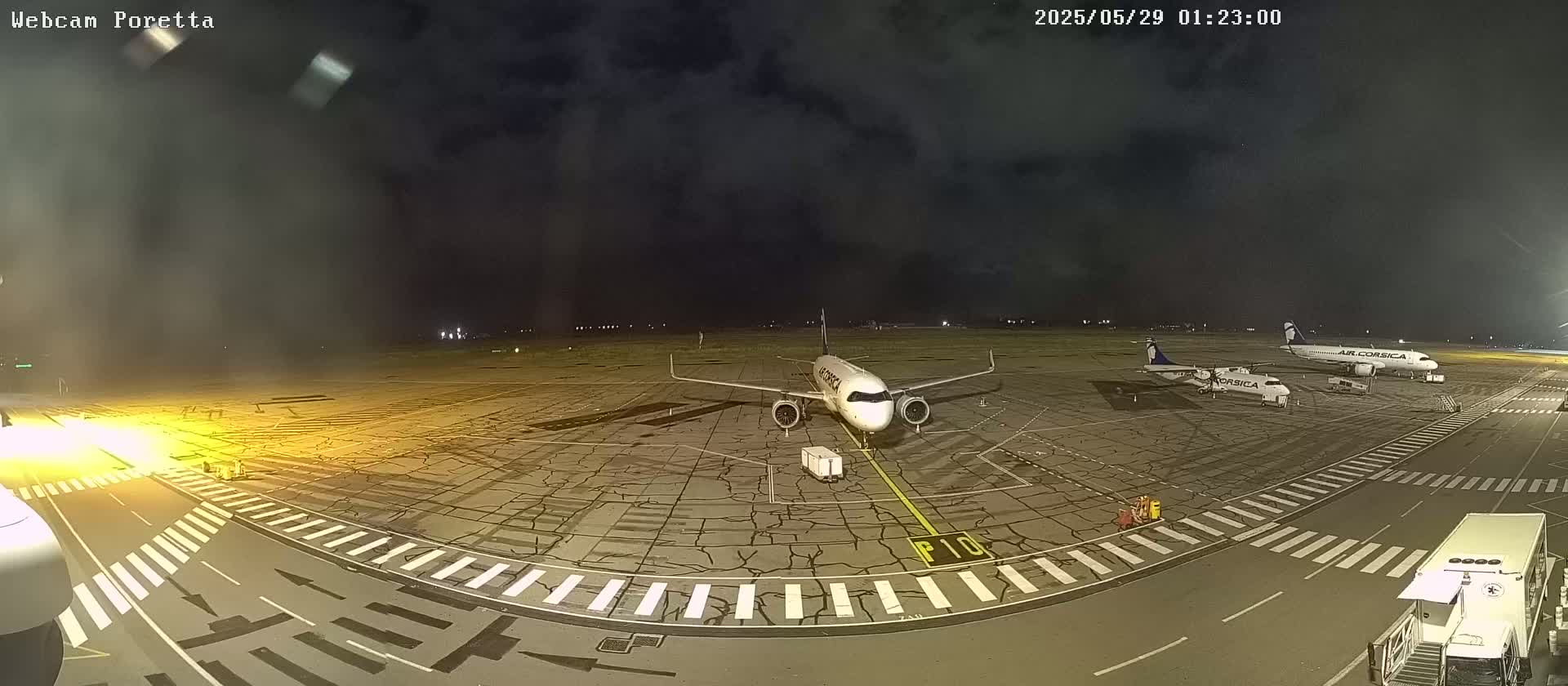 At night, under a cloudy sky, several airplanes are parked on a tarmac at an airport.