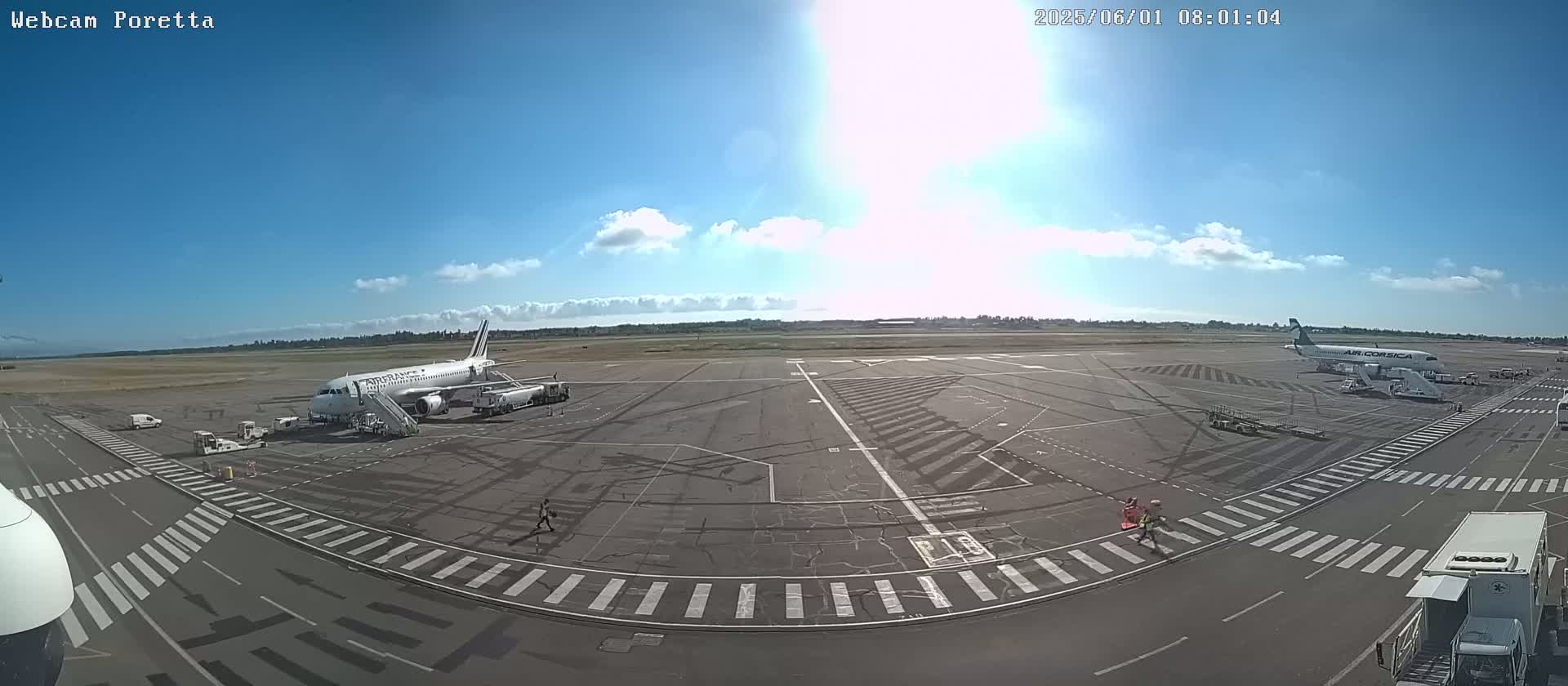 Two airplanes are parked on a sunny airport tarmac with a few people and ground support vehicles visible.