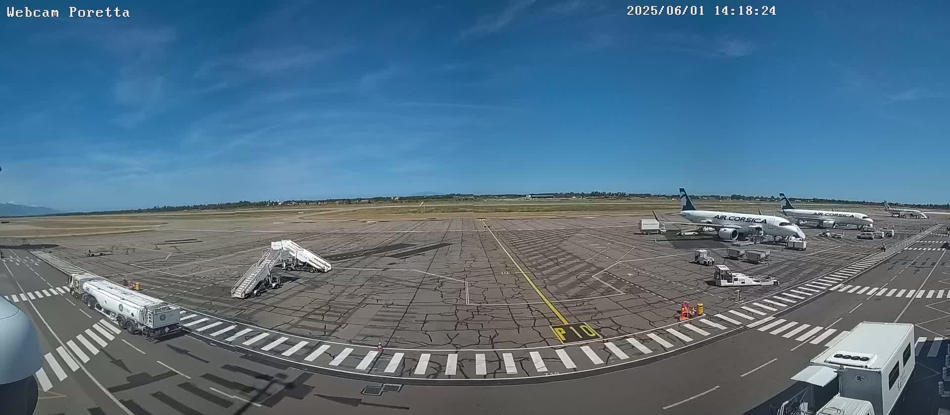 A sunny airport tarmac with several airplanes, ground support vehicles, and jet bridges.