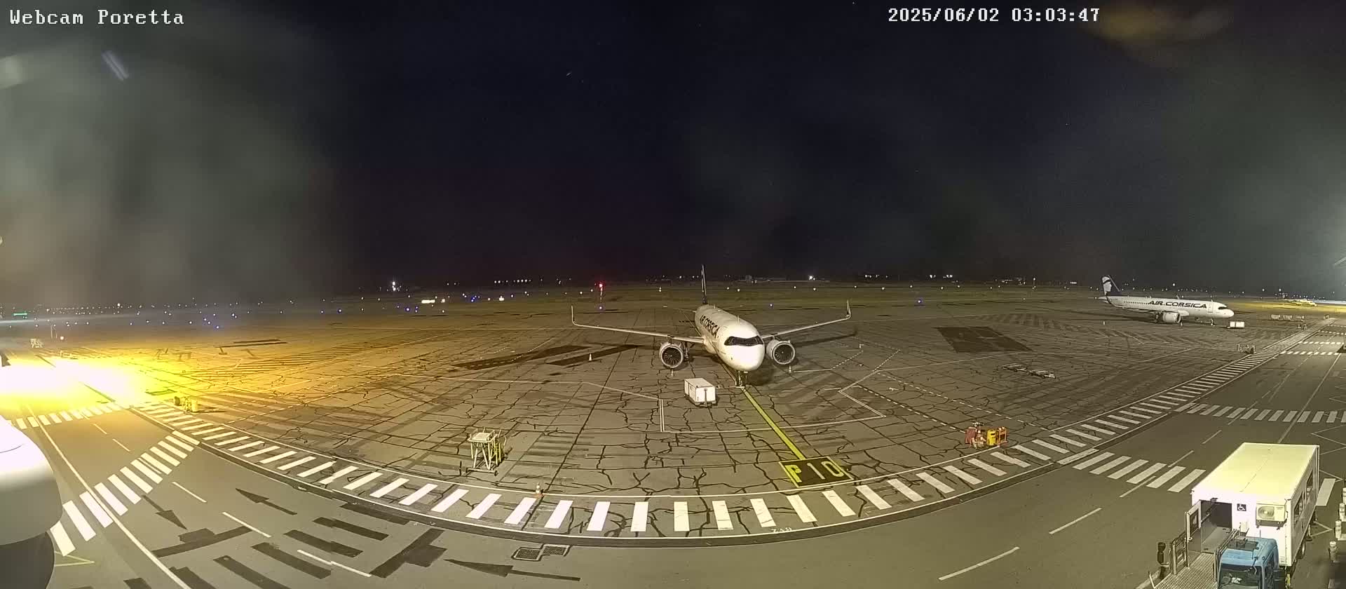 At night, a mostly empty airport tarmac shows an Air Corsica airplane parked near taxiways and a service vehicle.