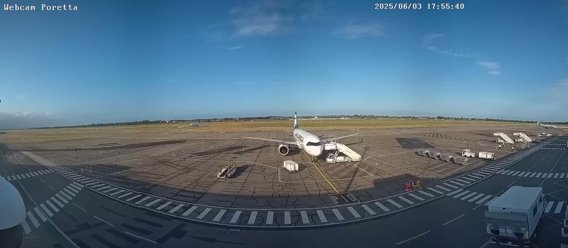 A passenger airplane is parked at an airport tarmac on a sunny day, with ground support equipment and other vehicles nearby.
