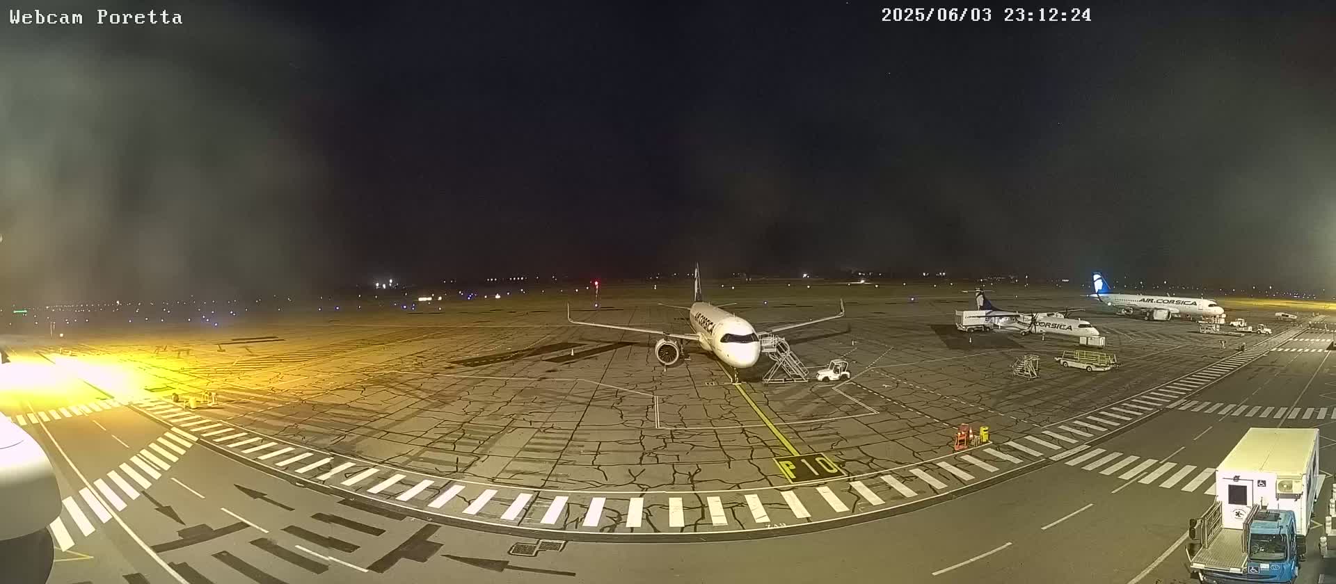 A nighttime view of an airport tarmac showing two airplanes parked near service vehicles, under a clear, dark sky.
