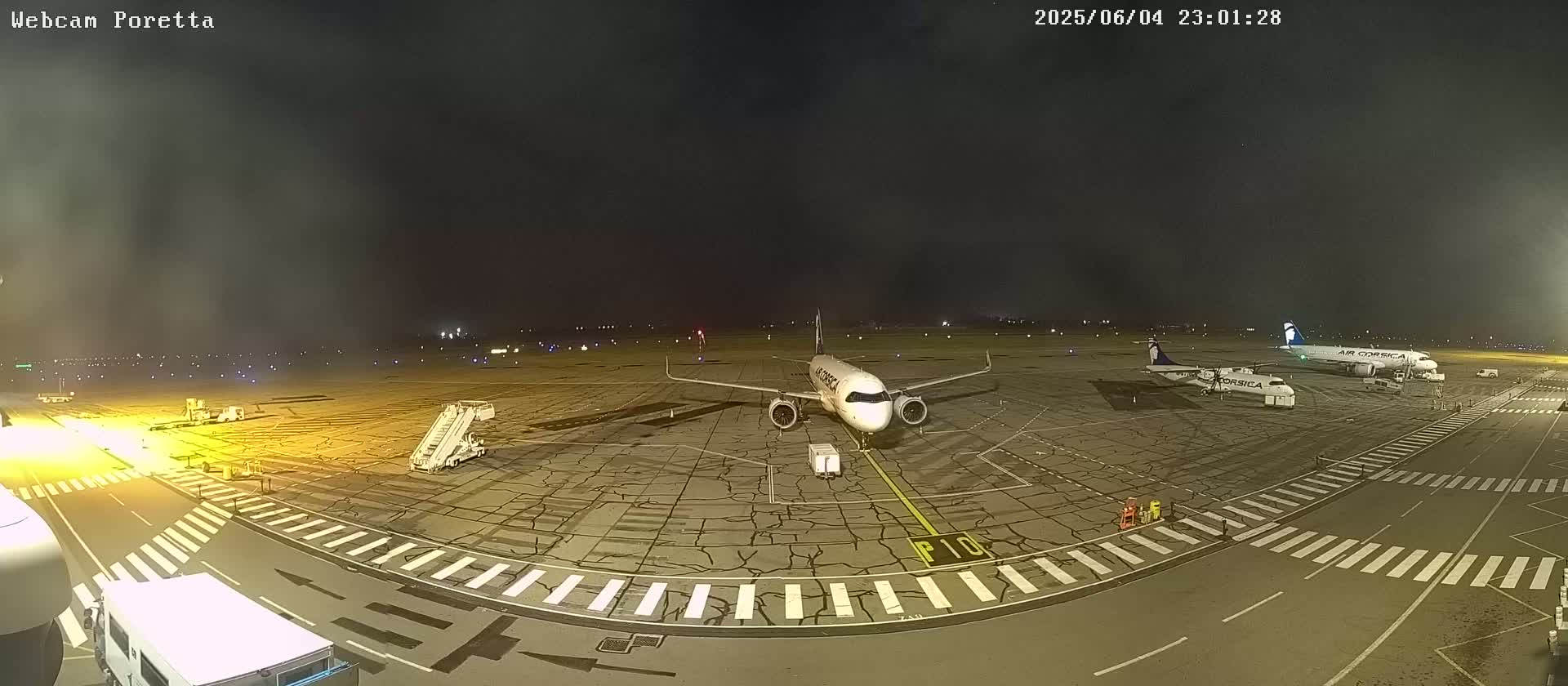 At night, under a hazy sky, several airplanes are parked on an airport tarmac with ground support equipment nearby.