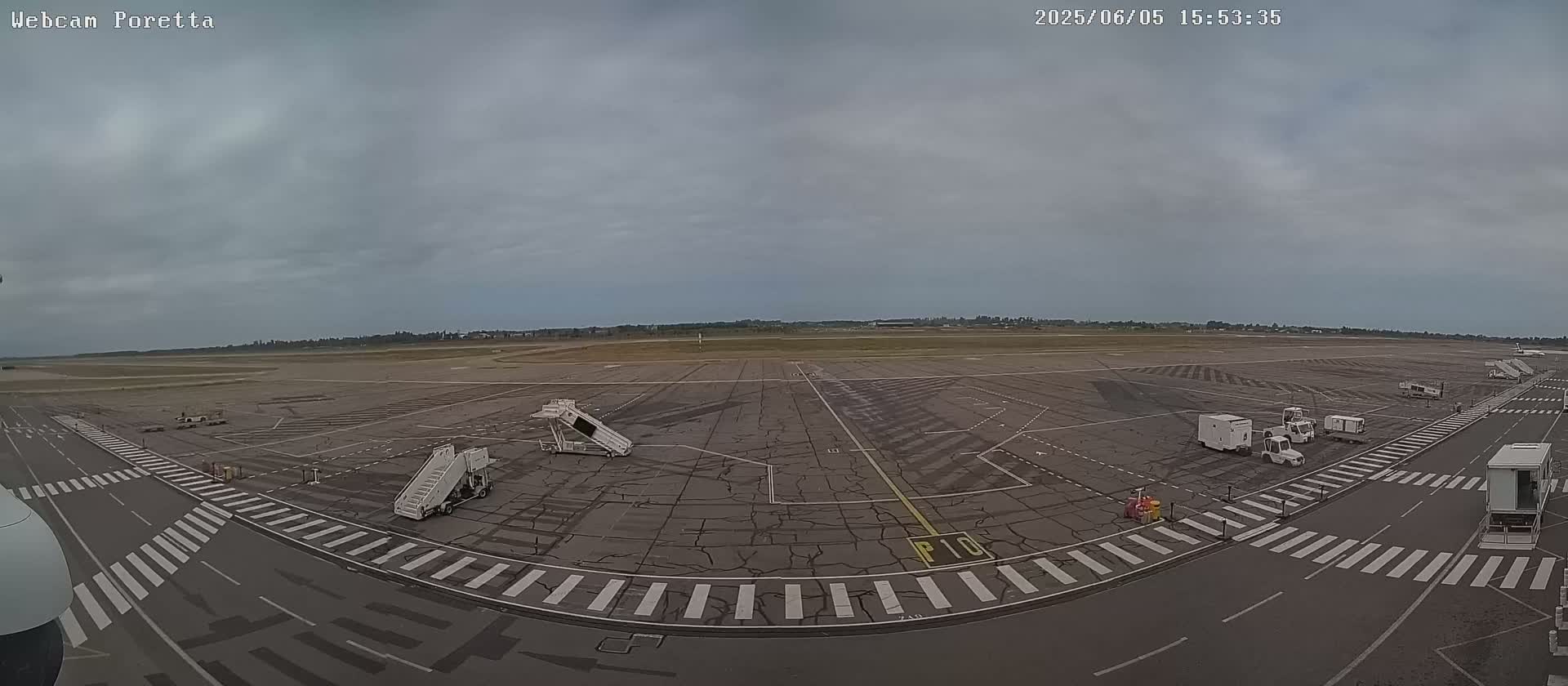 A mostly empty airport tarmac under an overcast sky, with a few ground service vehicles and passenger boarding bridges visible.