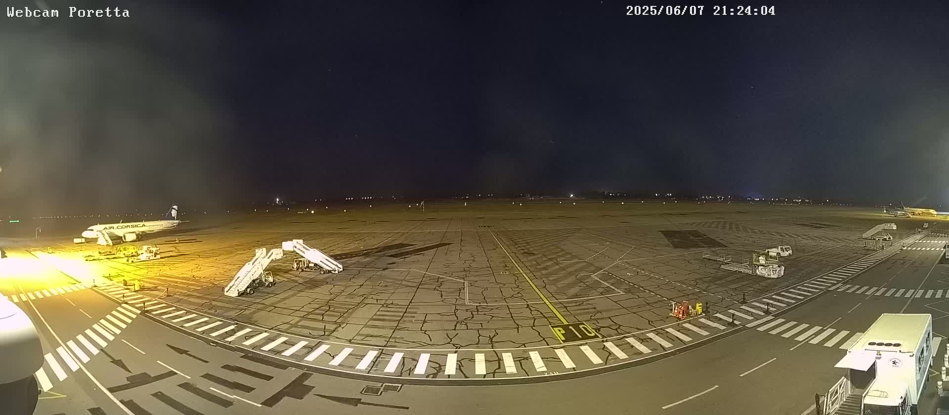 A nighttime view of an airport tarmac with an airplane at a gate, ground support equipment, and several vehicles.