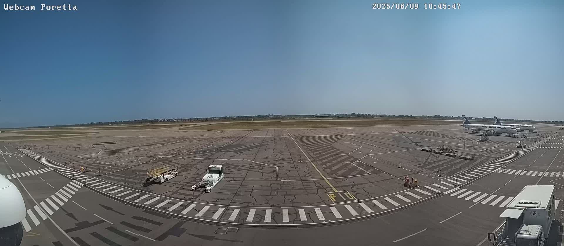 A tarmac at an airport on a clear, sunny day shows two airplanes parked and several airport vehicles on the ground.