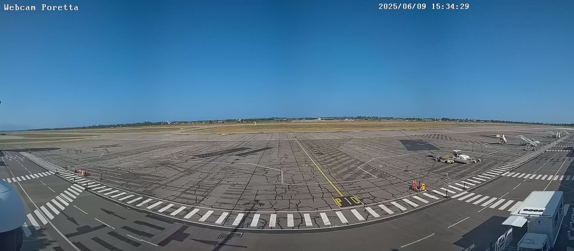 A wide, high-angle view shows a mostly empty airport tarmac under a clear blue sky.