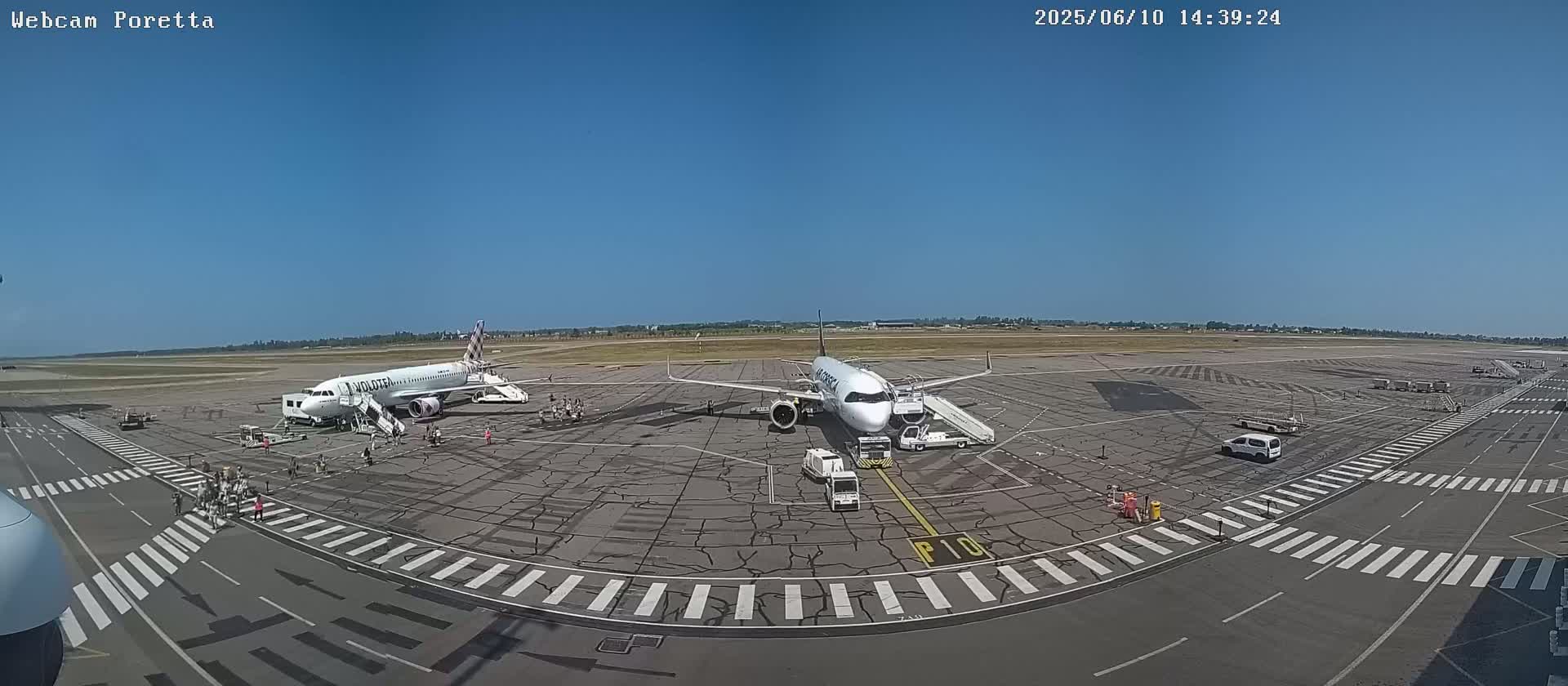Two airplanes are parked on a tarmac at an airport under a clear blue sky.