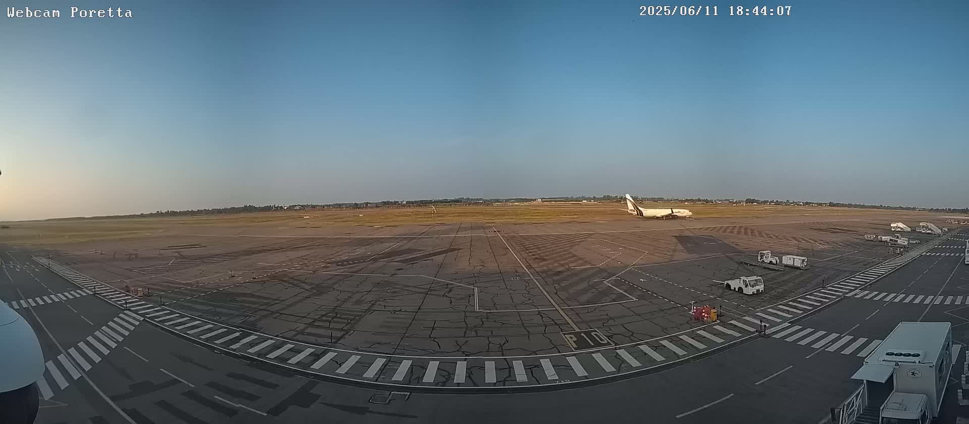 A large airplane sits on a tarmac at an airport under a clear, bright sky.