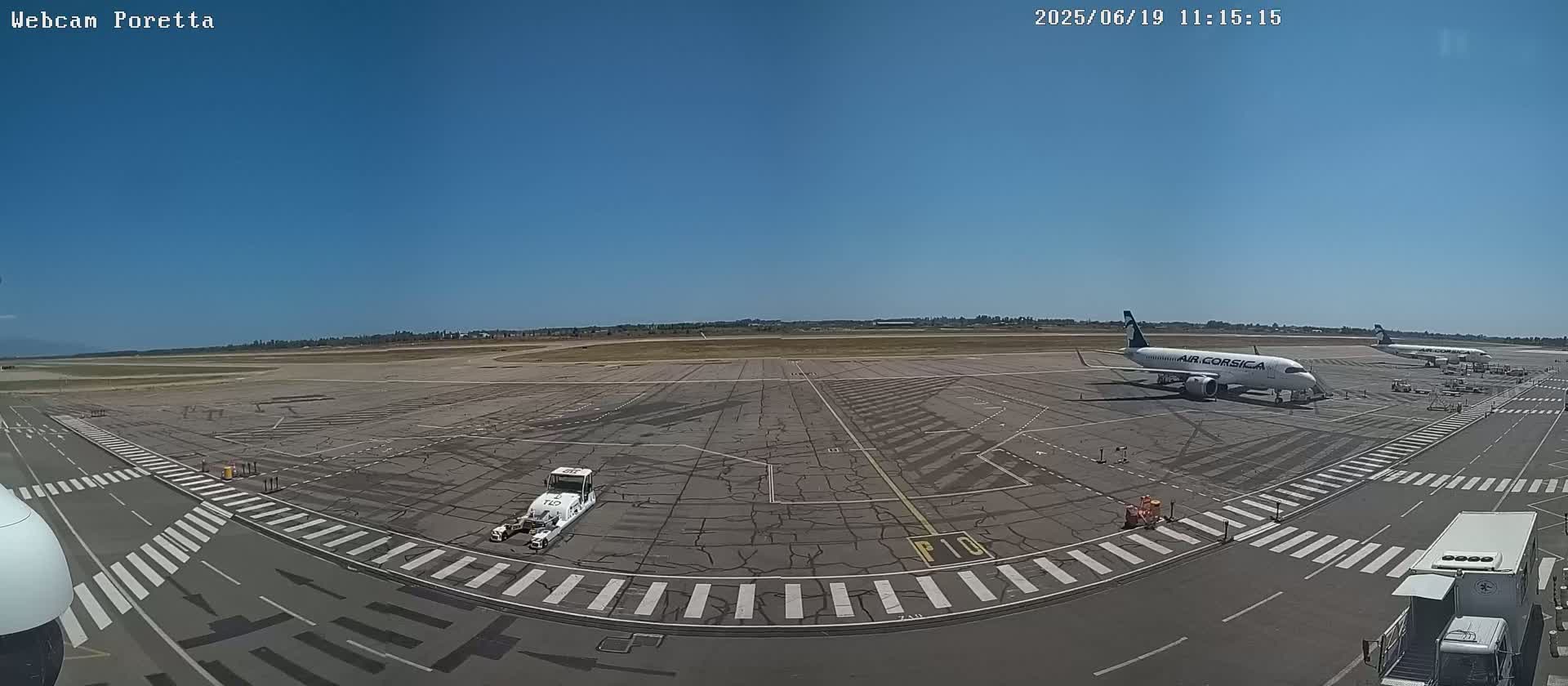 A sunny airport tarmac with several airplanes and ground support vehicles visible.