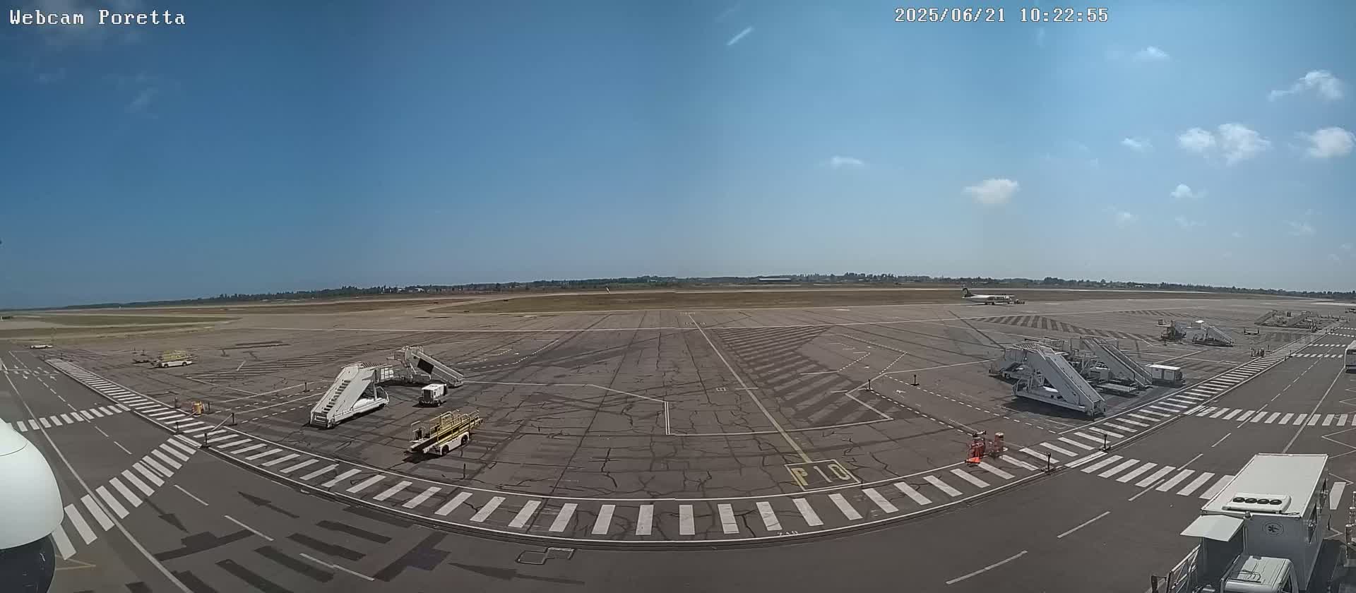 A mostly sunny airport tarmac with several jet bridges and support vehicles is visible, under a mostly clear sky.