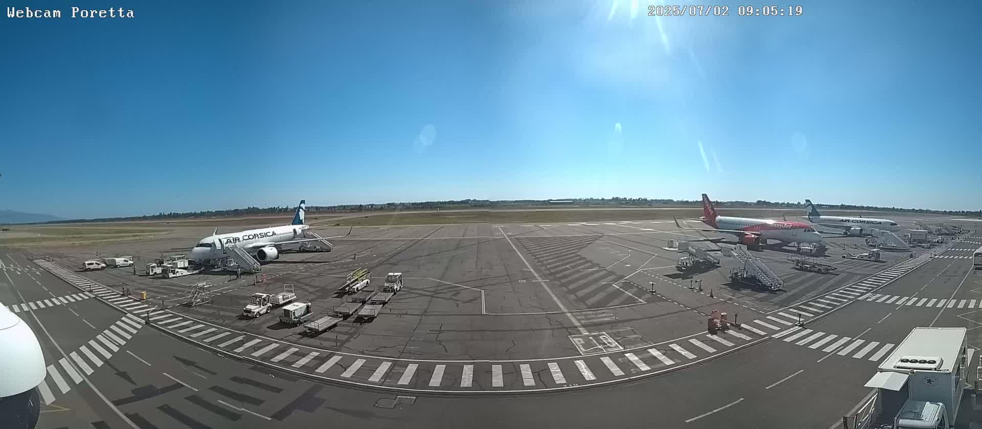 Several airplanes are parked at an airport tarmac on a sunny day.