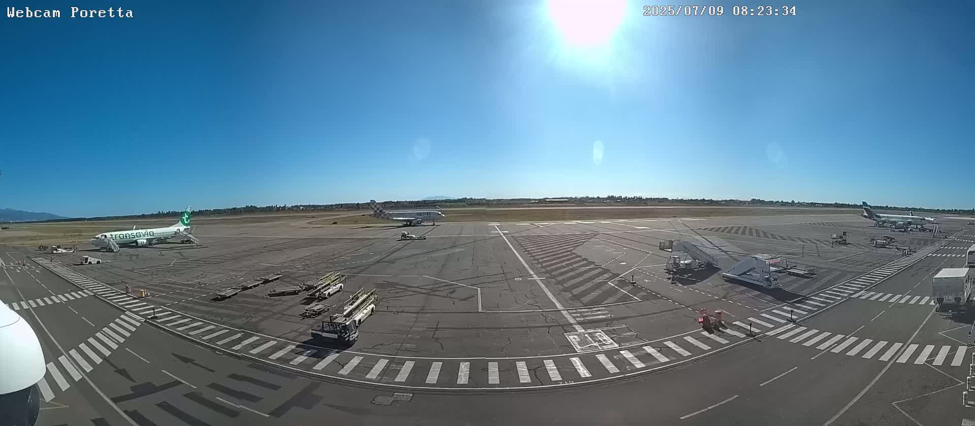 A sunny airport tarmac with several airplanes, ground support equipment, and marked roadways.