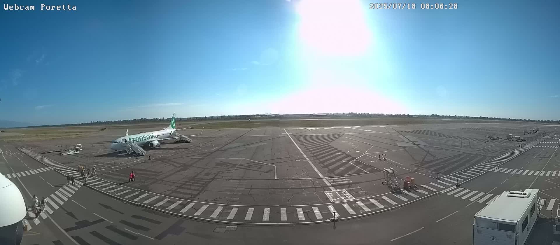 A passenger airplane sits on a tarmac under a bright, sunny sky.