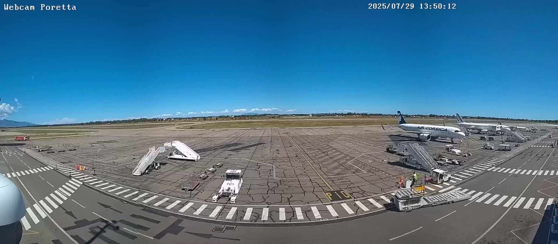 A sunny airport tarmac with several airplanes, ground support vehicles, and jet bridges.