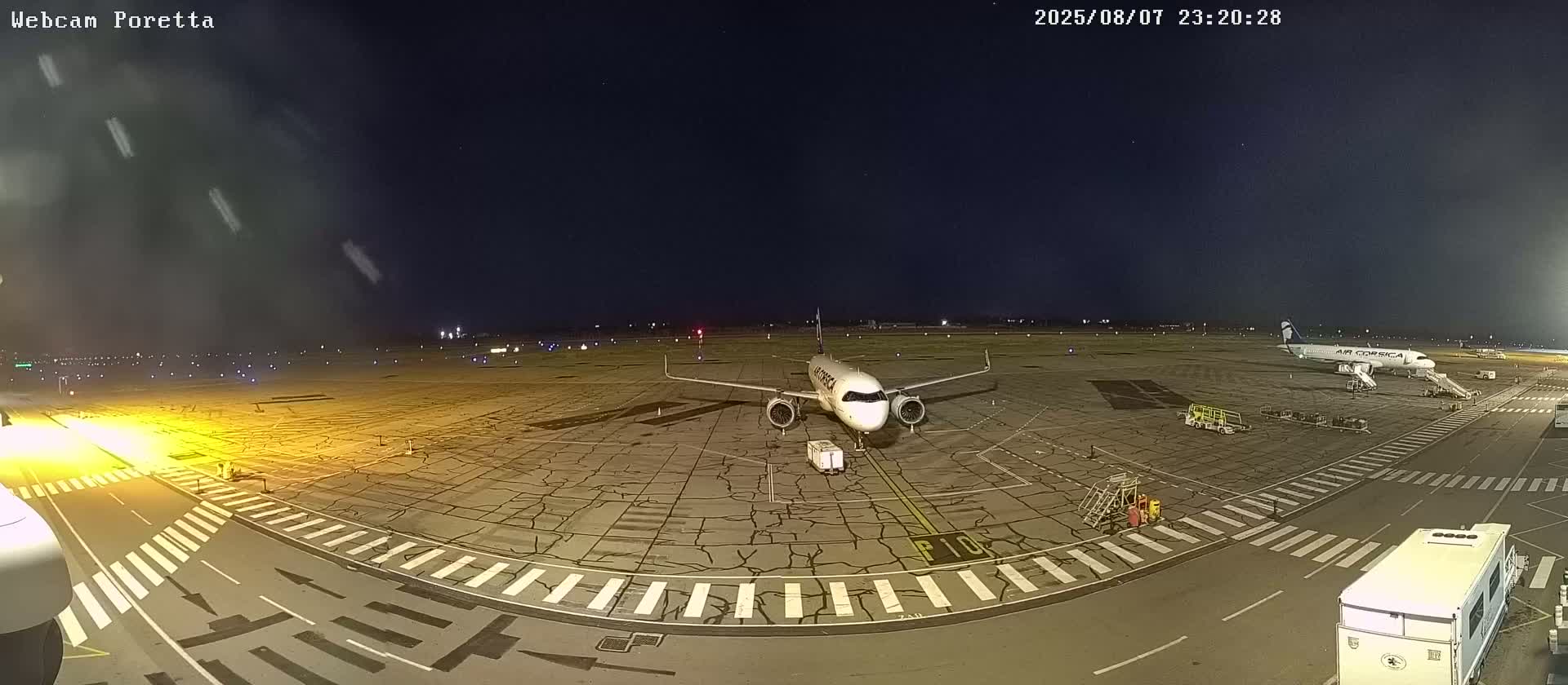 At night, under a clear sky, two airplanes are parked on a tarmac with service vehicles nearby.