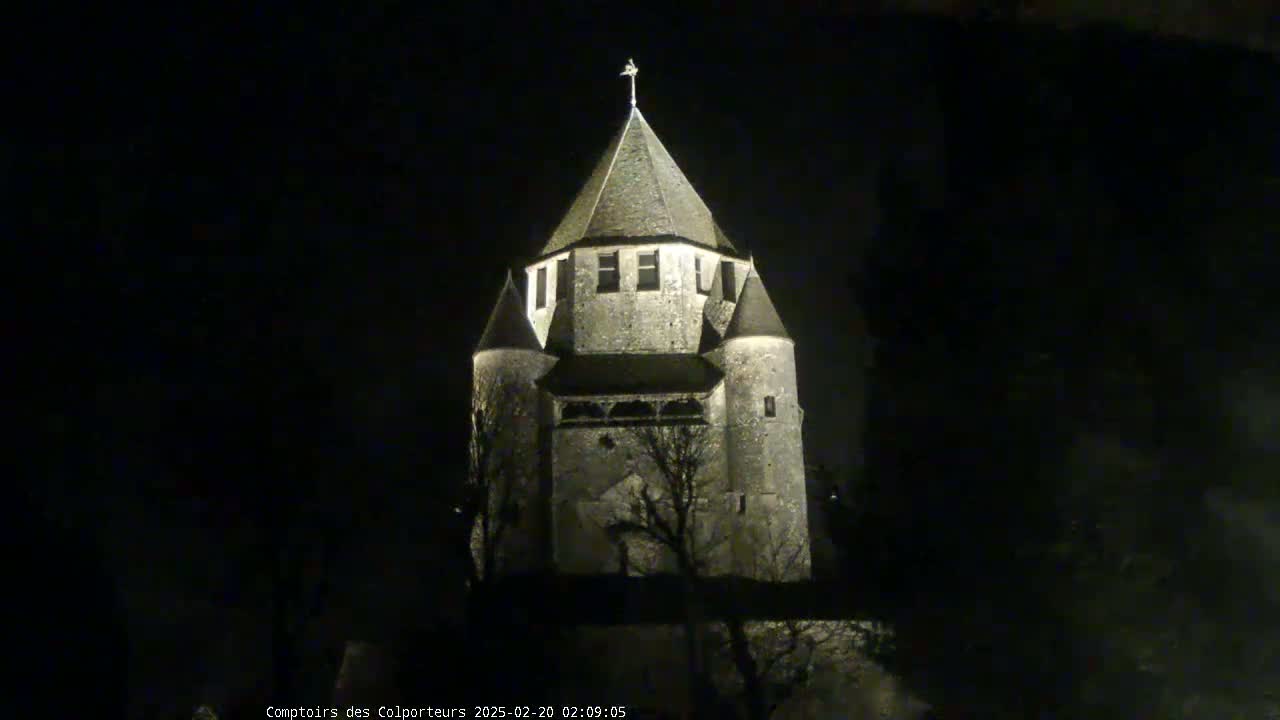 A stone tower, illuminated at night, stands against a dark, possibly overcast sky.