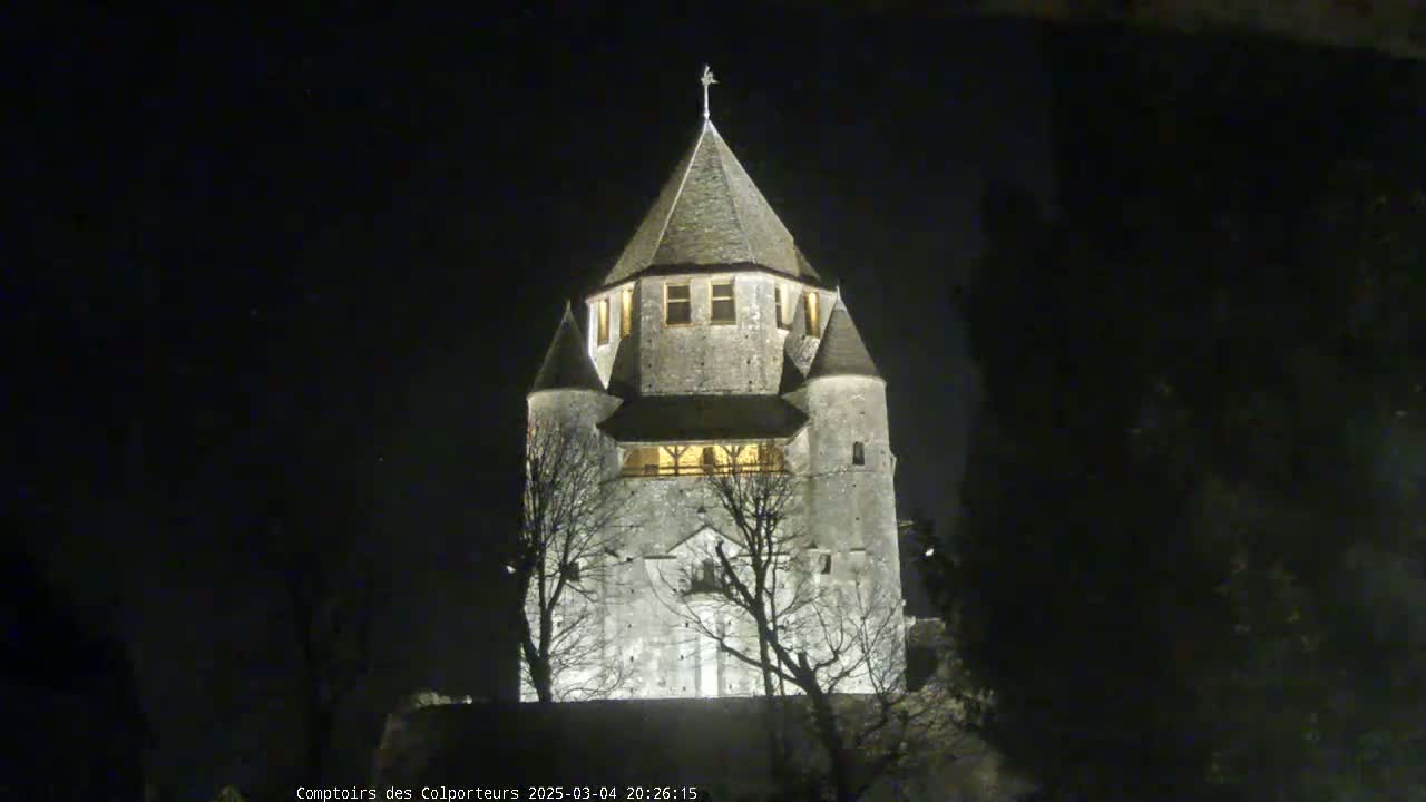 A tall, stone tower with a conical roof is illuminated at night, silhouetted against a dark sky.