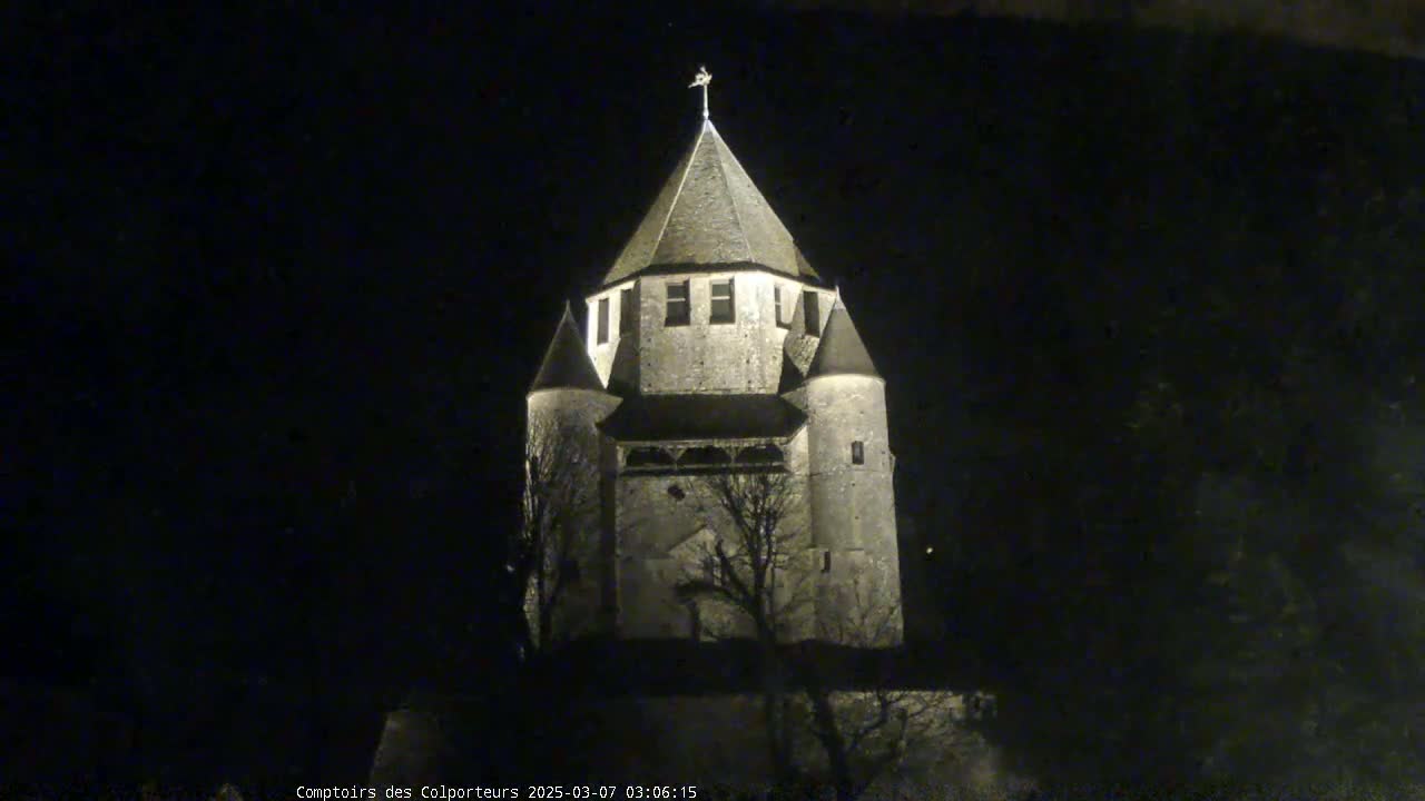 A stone tower, illuminated at night, stands against a dark background.