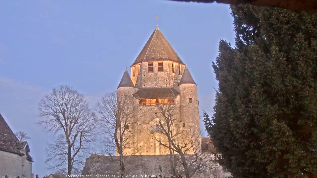 A tall, illuminated stone tower with a conical roof stands under a twilight sky, surrounded by bare trees.