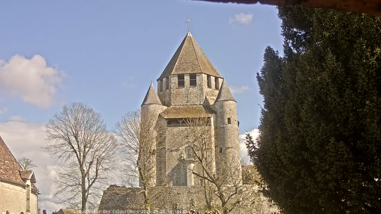 A stone tower with a conical roof, surrounded by bare trees under a partly cloudy blue sky.
