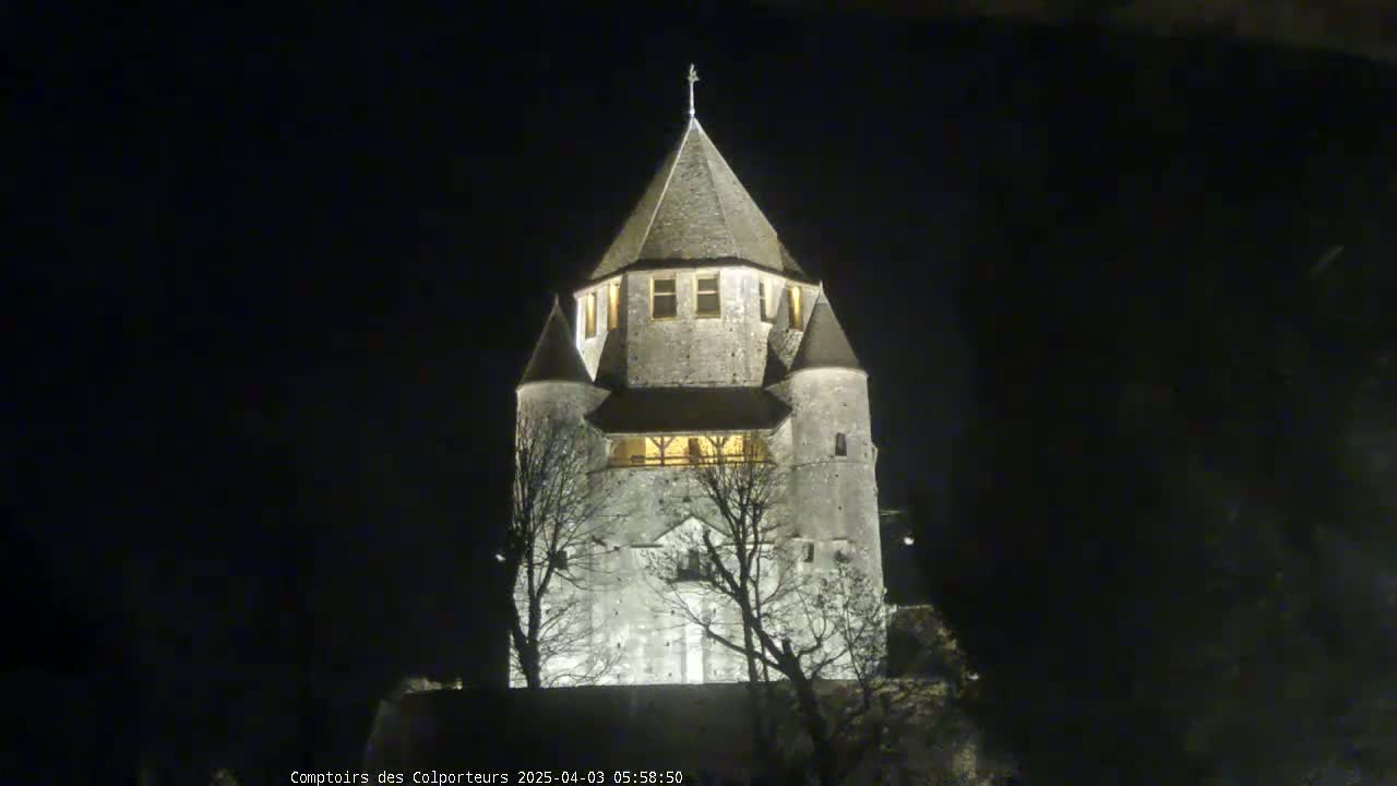 A tall, stone tower with a conical roof is illuminated at night, silhouetted against a dark sky.