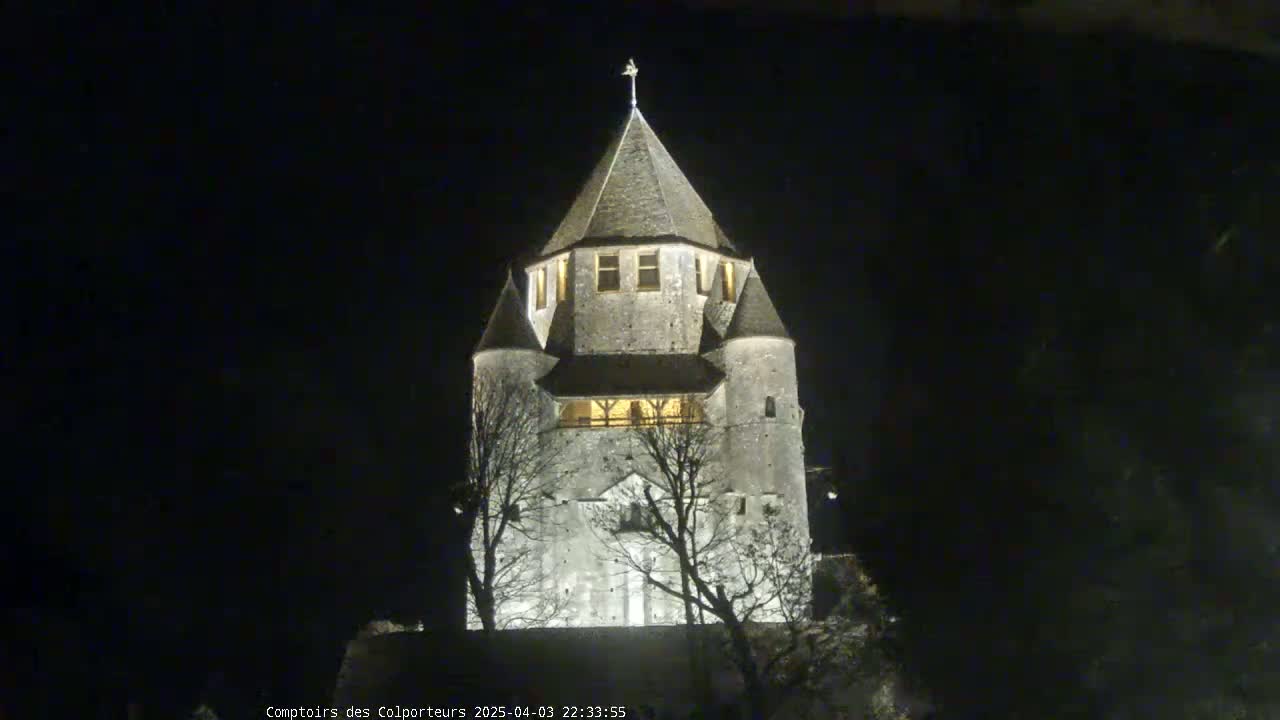 A tall, stone tower with a pointed roof is illuminated at night.