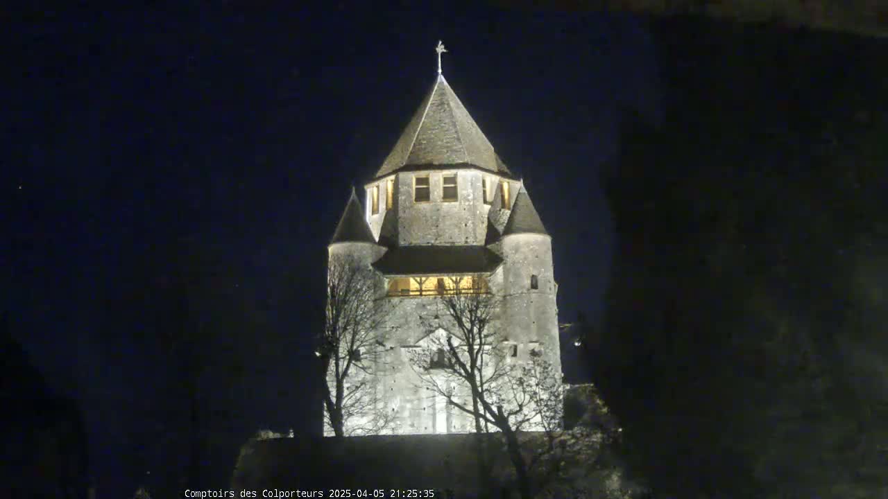 A tall, stone tower with a pointed roof is illuminated at night, silhouetted against a dark, clear sky.
