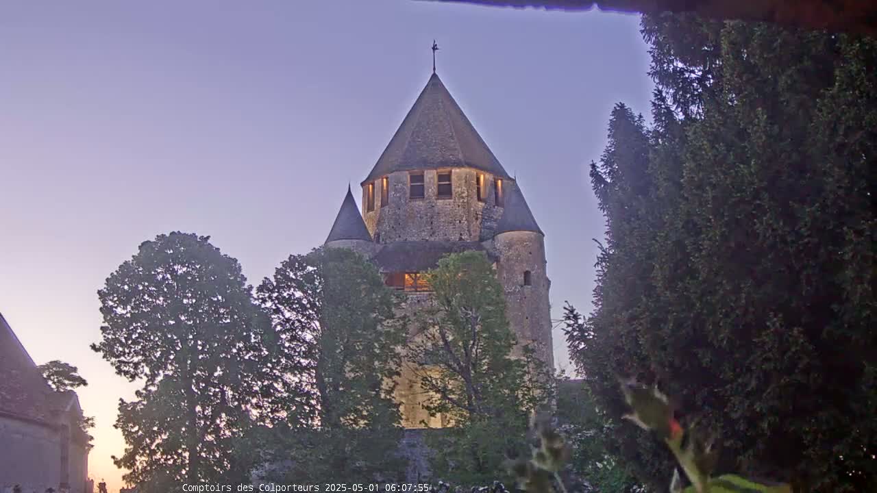 A stone tower, illuminated from within, stands among tall trees under a twilight sky.