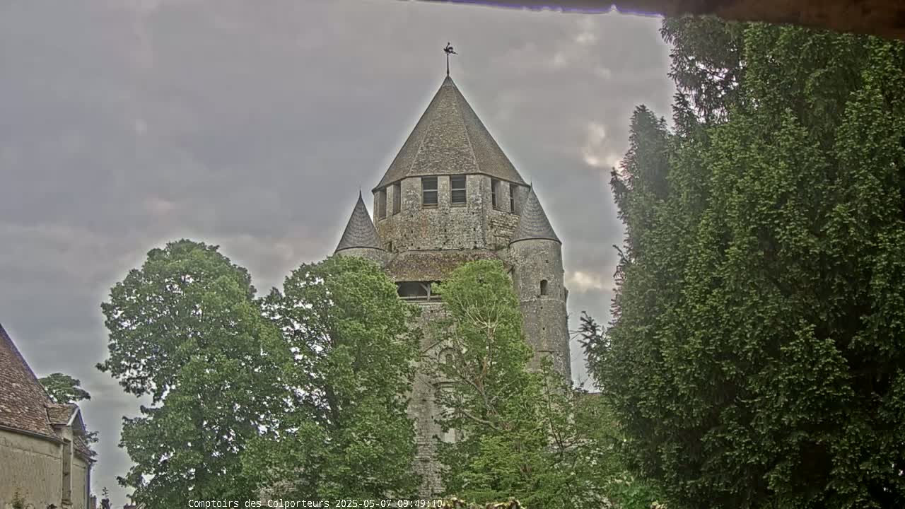 A stone tower, partially obscured by green trees, stands under a cloudy sky.
