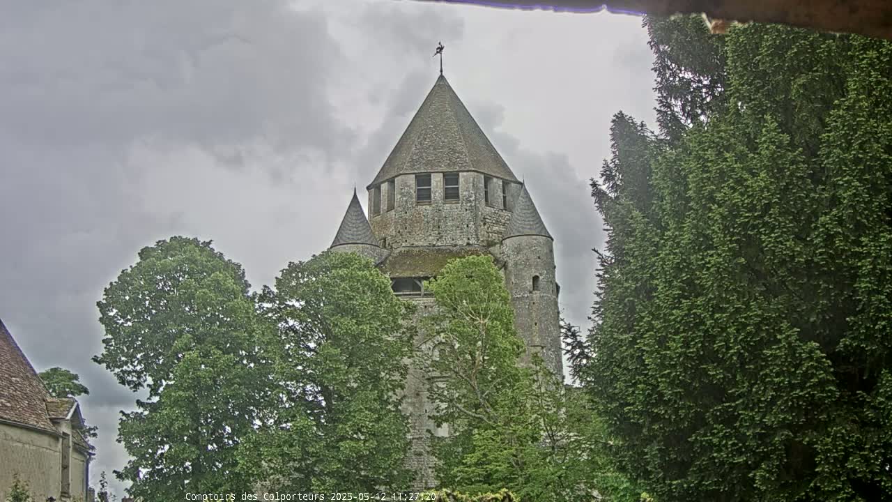 A stone tower with smaller flanking towers rises above green trees under a cloudy sky.