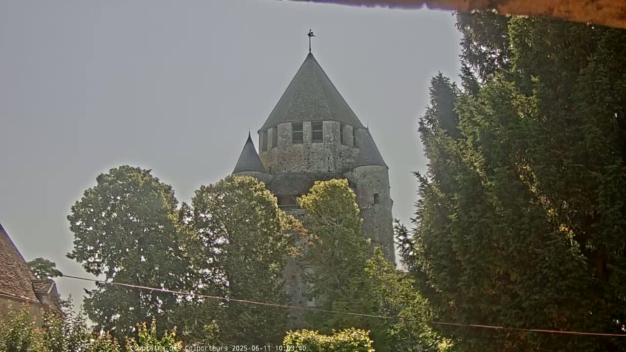 A stone tower, partially obscured by trees, stands under a mostly clear sky.