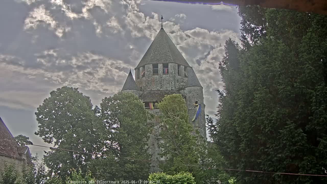 A stone tower, partially obscured by trees, stands under a partly cloudy sky.