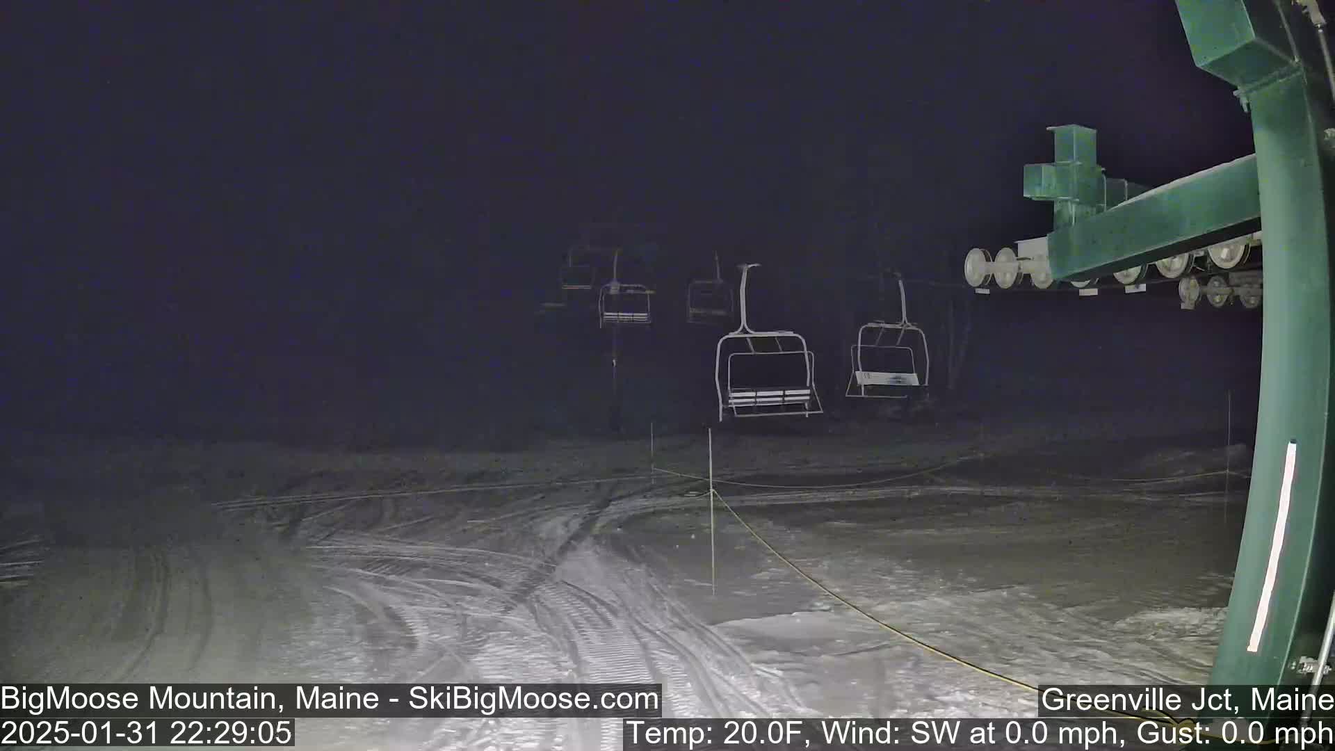 Empty ski lift chairs are visible at night on a snow-covered ski slope under calm, cold conditions.
