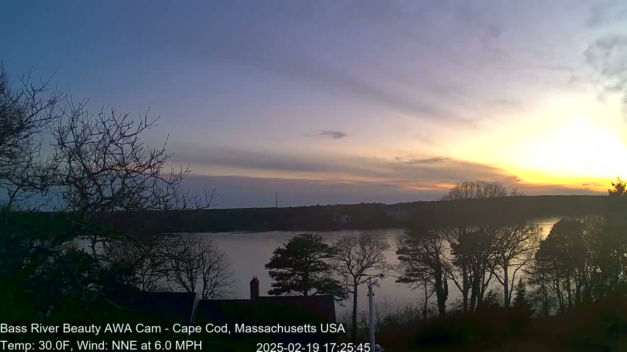 A calm river at sunset, with bare trees silhouetted against a pale orange and purple sky, under a 30°F temperature and a 6 mph NNE wind.