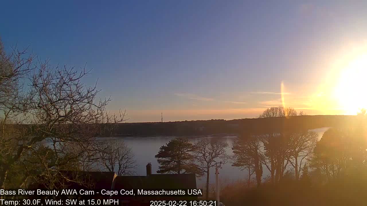 A sunset over a calm river, viewed from a wooded area with a southwest wind at 15 mph and a temperature of 30 degrees Fahrenheit.