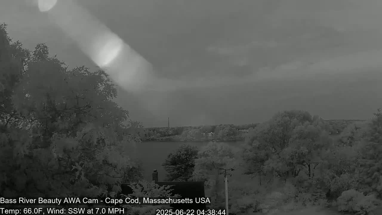 A grayscale view shows trees and a body of water under an overcast sky with a shaft of light breaking through the clouds, with a gentle south-southwesterly wind at 7 mph and a temperature of 66°F.
